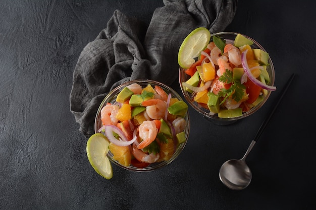 Ensalada de ceviche con camarones, naranjas y aguacate en recipiente de vidrio sobre un fondo oscuro o gris. Comida latinoamericana. Delicioso ceviche de camarones recién hecho. Camarones marinados en lima y naranja.