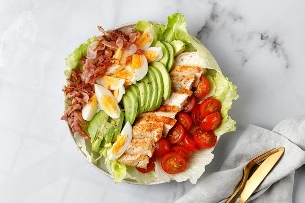 Ensalada Cobb con aguacate, tomate, huevos de pollo a la parrilla, tocino sobre fondo blanco de mármol Dieta Keto