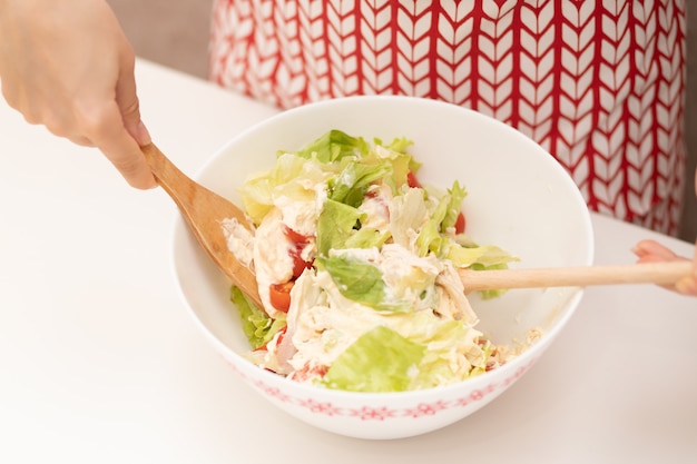 Ensalada de cocina Las manos femeninas mezclan los ingredientes.