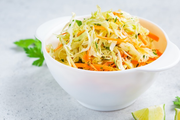 Ensalada de col fresca con col y zanahorias en un tazón blanco.