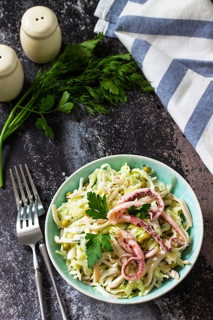 Ensalada con col fresca, pepino, guisantes verdes y pulpo en un bol sobre una encimera oscura. Copiar espacio.