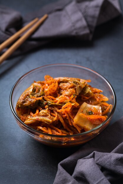 Ensalada de col kimchi coreano tradicional orgánica casera con palillos en una mesa oscura. Concepto de alimentos saludables para el intestino conservado vegetariano fermentado, vegano