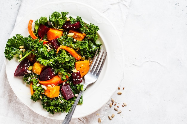 Ensalada de col rizada con verduras al horno en plato blanco.