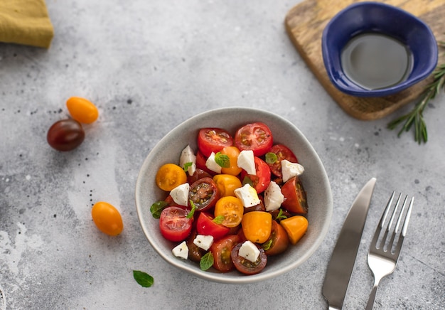 Ensalada con coloridos tomates cherry, queso feta, hierbas, aceite de oliva, comida mediterránea, superficie de concreto gris,