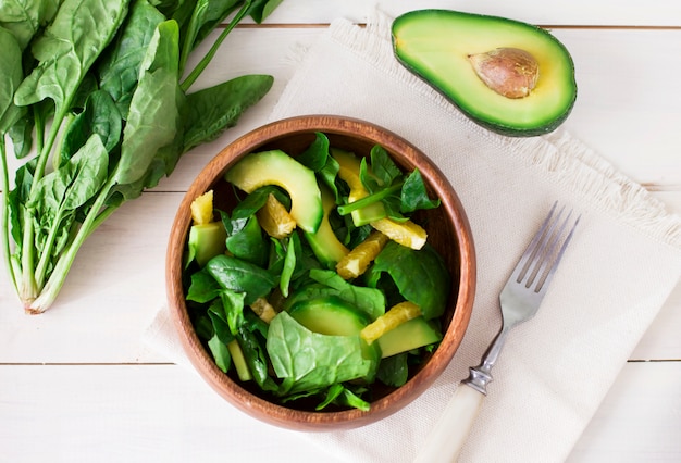 Ensalada cruda de espinaca, aguacate y naranja en plato de madera sobre fondo blanco