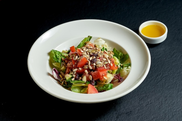 Ensalada dietética con tomates y pepinos, semillas en un plato blanco sobre fondo negro