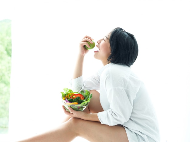 Ensalada eatiing asiática de la mujer joven en la comida blanca de la dieta del fondo