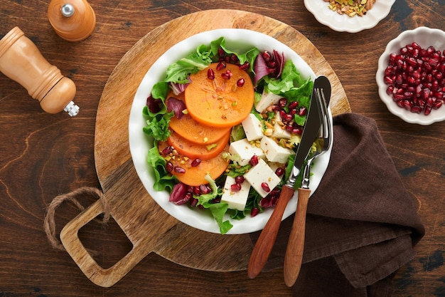 Ensalada Ensalada verde fresca con queso feta, caqui, granada y pistacho en un plato blanco Idea para una deliciosa y saludable ensalada navideña de invierno Una alimentación sana y equilibrada Vista superior