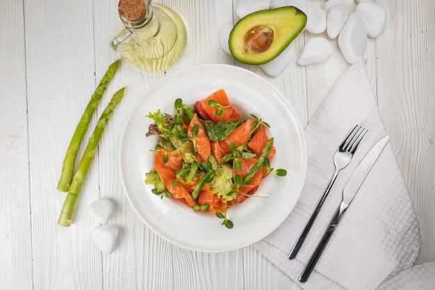 Ensalada de espárragos y verduras de salmón en un plato blanco y mesa blanca