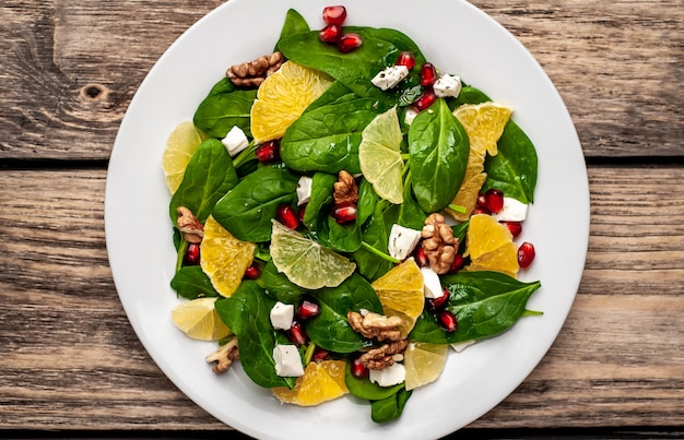 Ensalada de espinacas, naranja, limón, granada, queso feto, nuez en un plato blanco sobre una mesa de madera