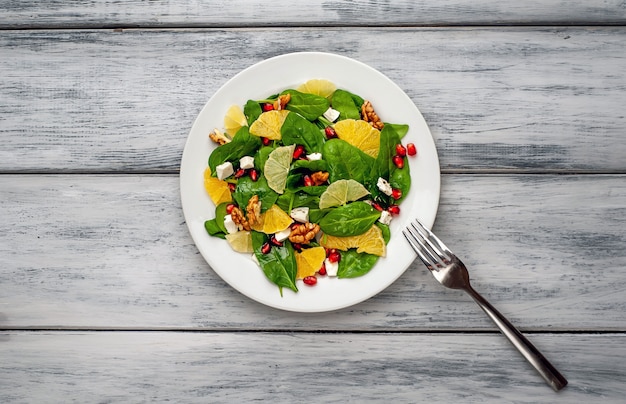 Ensalada de espinacas, naranja, limón, granada, queso feto, nuez en un plato blanco sobre una mesa de madera