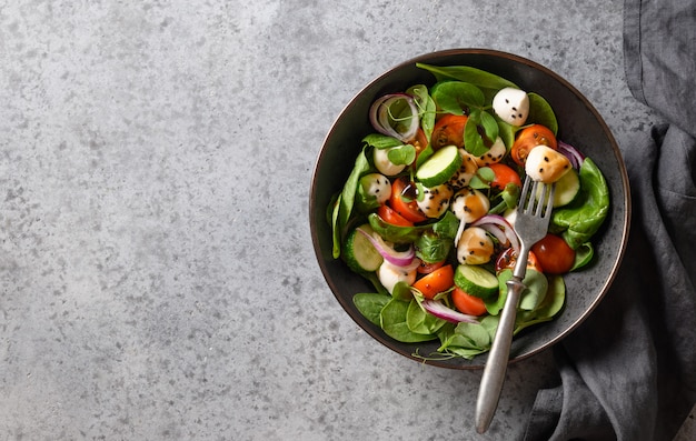 Ensalada de espinacas, tomates cherry, cebolla y mozzarella sobre fondo de piedra gris. Vista superior.