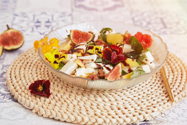 Ensalada estética francesa vegetariana con mango feta flores comestibles higos melocotón albahaca sobre fondo de baldosas de cerámica Comida saludable