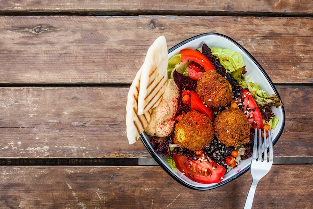 Ensalada de falafel con hummus, remolacha y verduras en un recipiente en la mesa de madera, vista superior.