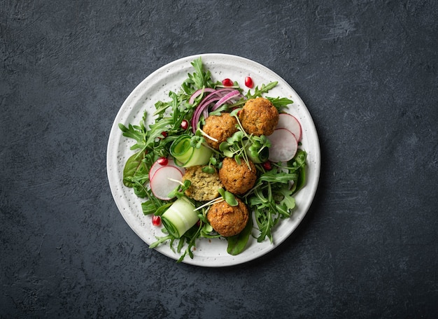 Ensalada de falafel y verduras frescas en un plato de cerámica blanca sobre una mesa oscura, vista superior.