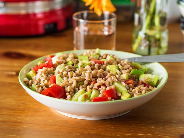 Foto ensalada de farro spelt italiana fresca con tomates aguacate y pepinos en la mesa de madera de la cocina