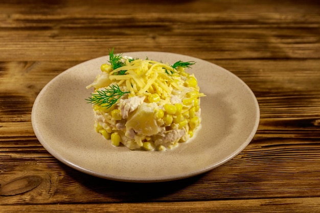 Ensalada festiva con pechuga de pollo, maíz dulce, piña enlatada, queso y mayonesa sobre mesa de madera