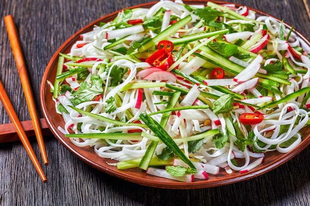 Ensalada de fideos de arroz y verduras en un plato sobre una mesa de madera, cocina china, vista horizontal desde arriba