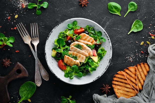 Ensalada con filete de pollo, aceitunas, tomates y aguacates en un plato sobre un fondo de madera Vista superior Espacio libre para su texto Plano