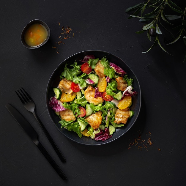 Ensalada con filete de pollo, naranjas, tomates cherry y lechuga. Vista superior de fondo oscuro