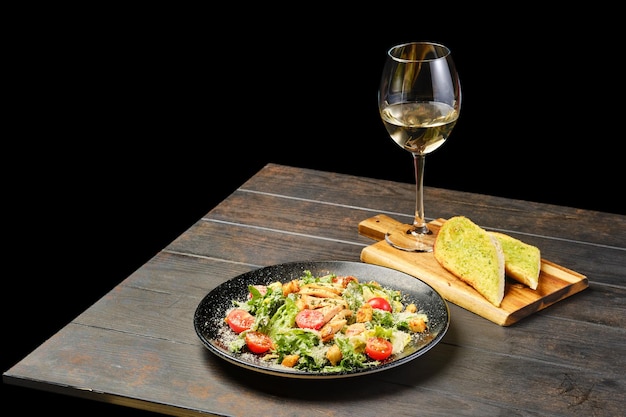 Ensalada con filete de pollo tomate y queso con copa de vino blanco sobre una mesa