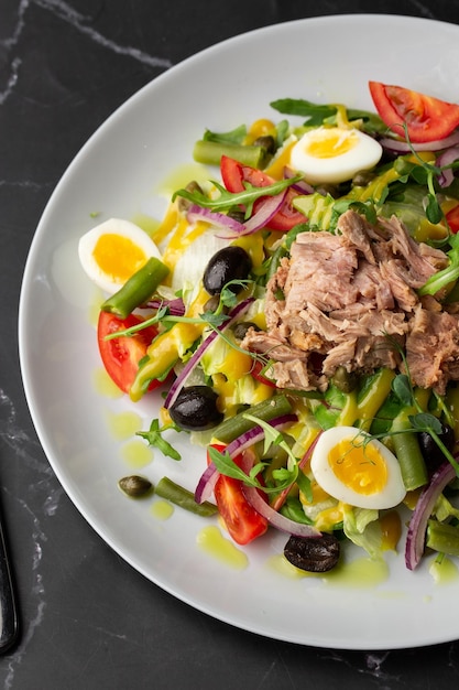 Ensalada francesa Nicoise con huevo de atún judías verdes tomates aceitunas lechuga cebolla y anchoas sobre un fondo gris Comida saludable