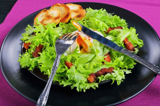 Ensalada francesa tradicional Lyonnaise con lechuga frisee, tocino y huevo escalfado