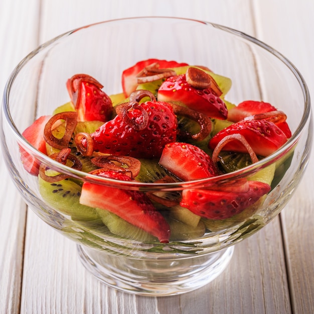 Ensalada de fresas, kiwi, espinacas sobre un fondo de madera blanca.