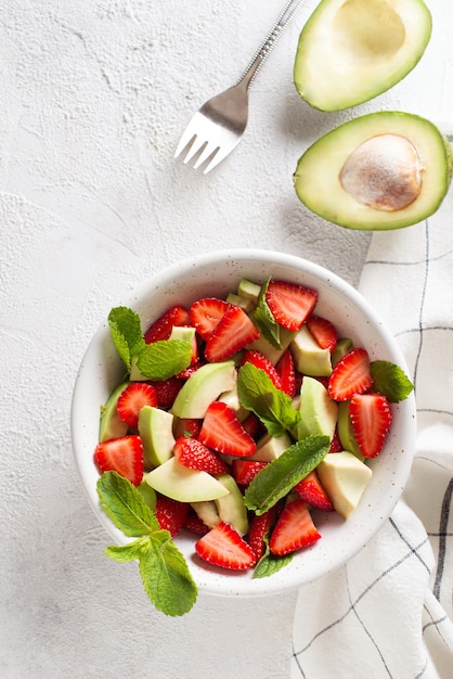 Ensalada fresca de aguacate y fresa con hojas de menta sobre fondo blanco.