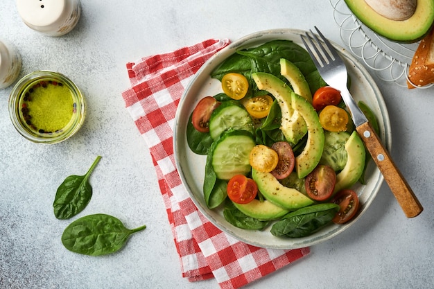 Ensalada fresca de aguacate, tomate cherry rojo, amarillo, negro, espinacas y pepino con especias, pimienta y aceite de oliva en un tazón gris sobre fondo gris pizarra, piedra u hormigón. Concepto de comida sana. Vista superior.