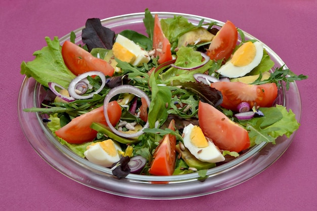 Ensalada fresca apetitosa con tomates y hierbas y aguacates en un plato sobre un fondo morado