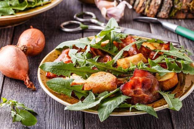 Ensalada fresca de diente de león con tocino frito y picatostes de ajo.