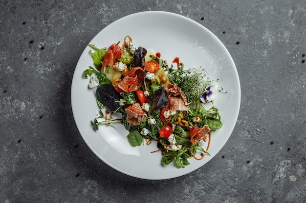 Ensalada fresca con jamón y pera sobre un fondo gris oscuro. ensalada de jamón, mezcla de ensalada, espinacas, pera, tomates cherry