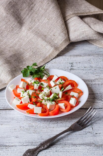 Ensalada fresca con mozzarella de tomate y hierbas sobre fondo blanco de madera