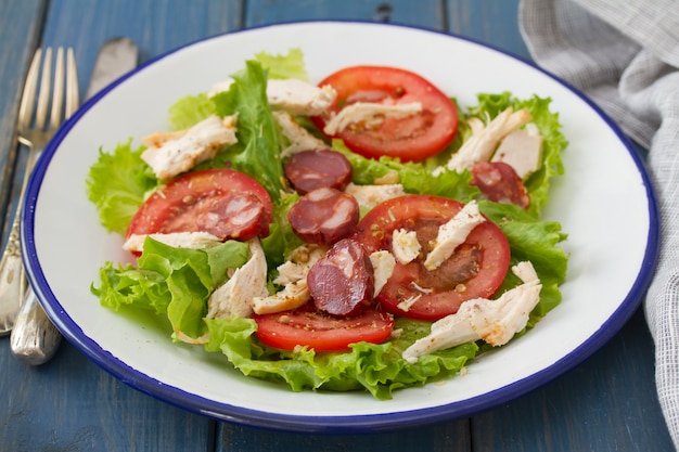 Ensalada fresca con pollo y chourico en plato blanco sobre mesa de madera azul