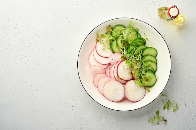 Ensalada fresca con rábano rojo, pepino, verduras, rábanos microverdes en plato blanco