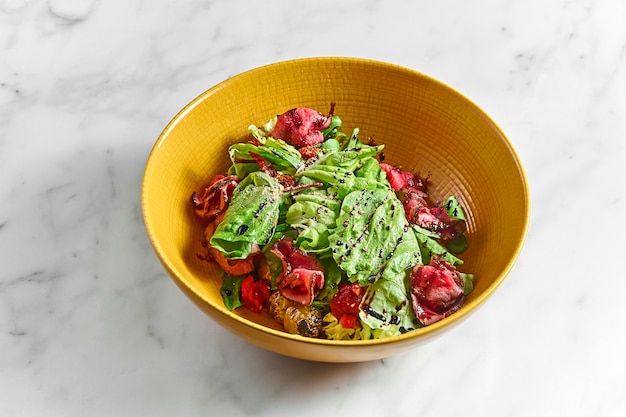 Ensalada fresca con rodajas de rosbif medio raro, con tomates cherry en un recipiente amarillo sobre una mesa de mármol blanco