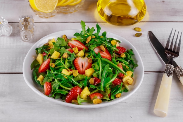 Ensalada fresca con rúcula, fresas, piña y pistachos servidos en plato blanco sobre mesa de madera rústica