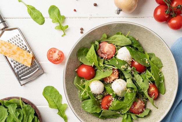 Ensalada fresca con rúcula, tomates cherry, queso mozzarella y queso duro sobre fondo blanco de madera Vista superior