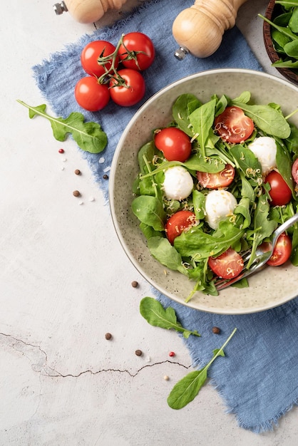 Ensalada fresca con rúcula, tomates cherry, queso mozzarella y queso duro sobre fondo blanco de madera Vista superior