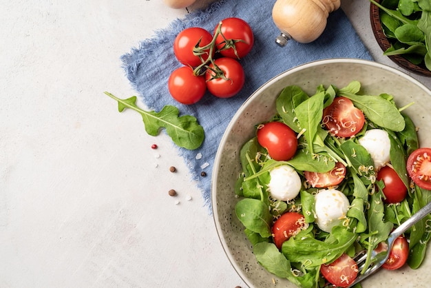 Ensalada fresca con rúcula, tomates cherry, queso mozzarella y queso duro sobre fondo blanco de madera Vista superior