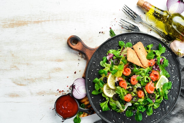 Ensalada fresca con salmón y aceitunas en plato negro. Vista superior. Espacio libre para su texto. Estilo rústico.