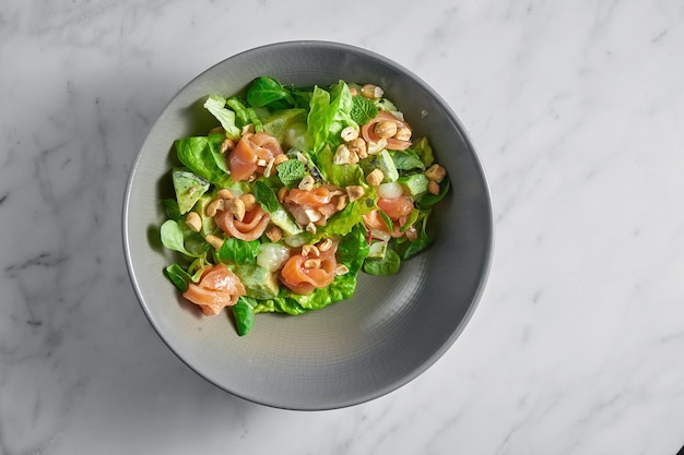 Ensalada fresca con salmón, queso delicado, maní y menta en un recipiente gris sobre mármol blanco