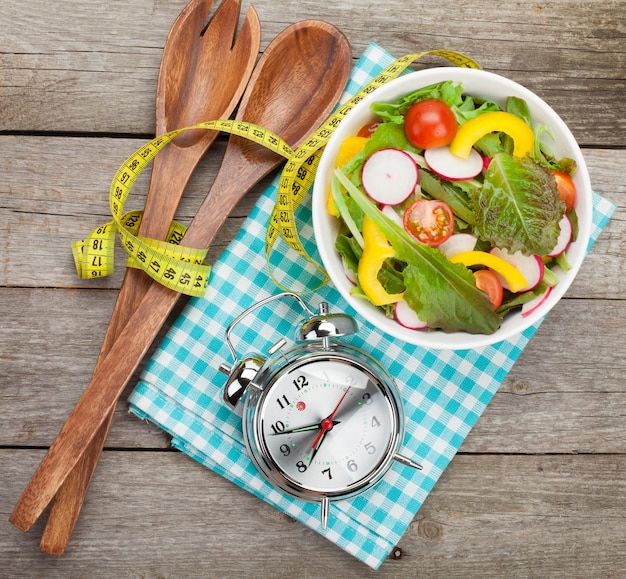 Ensalada fresca y saludable y cinta métrica en la mesa de madera