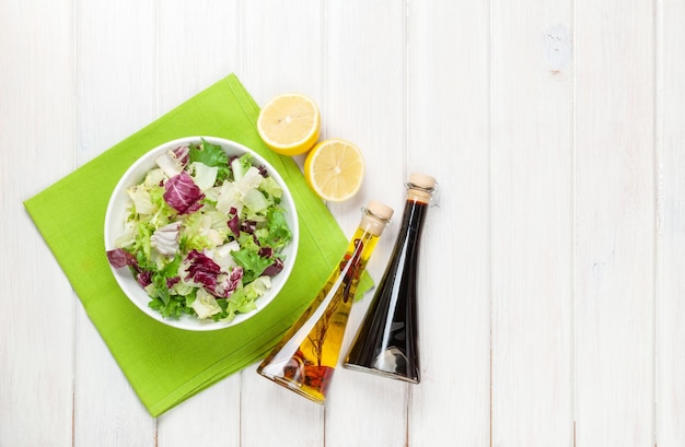 Ensalada fresca y saludable y condimentos sobre una mesa de madera blanca