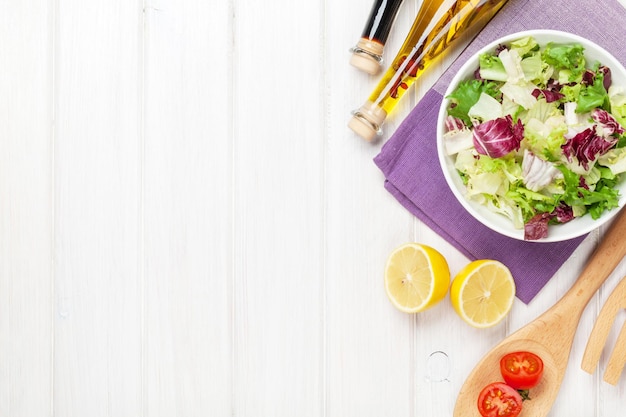 Ensalada fresca y saludable y condimentos sobre una mesa de madera blanca