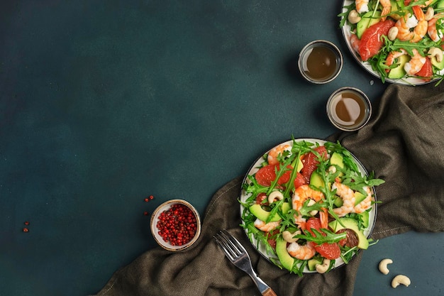 Ensalada fresca y saludable con gambas, aguacate, pomelo, rúcula y anacardos. Fondo de la mesa de la cocina verde oscuro. Vista superior del espacio de copia.