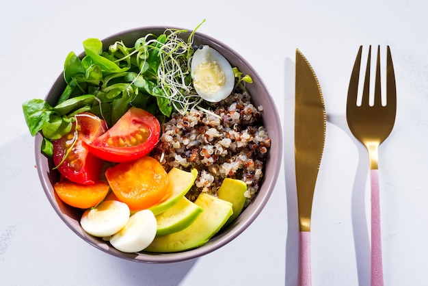 Ensalada fresca y saludable con quinua, tomates cherry y verduras mixtas, aguacate, huevo y microgreens en mármol