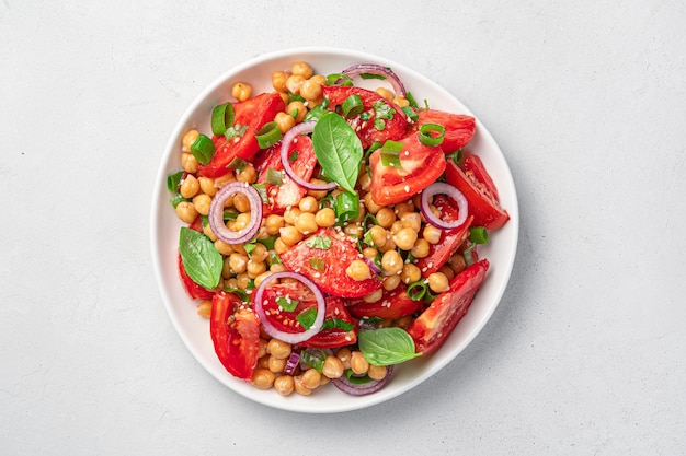 Ensalada fresca y saludable con tomates, garbanzos, albahaca y sésamo sobre un fondo gris. Vista superior, primer plano. Comida vegetariana.