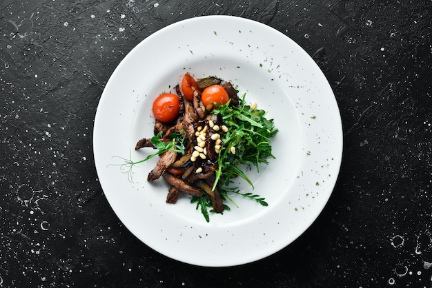 Ensalada fresca con ternera, rúcula, piñones de ternera y berenjena, comida saludable en un plato blanco de estilo rústico